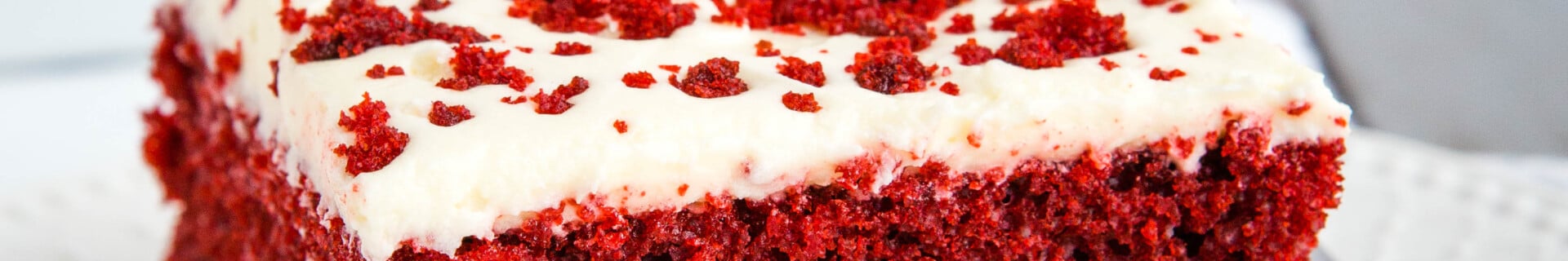 slice of homemade red velvet cake with cream cheese frosting on white plate