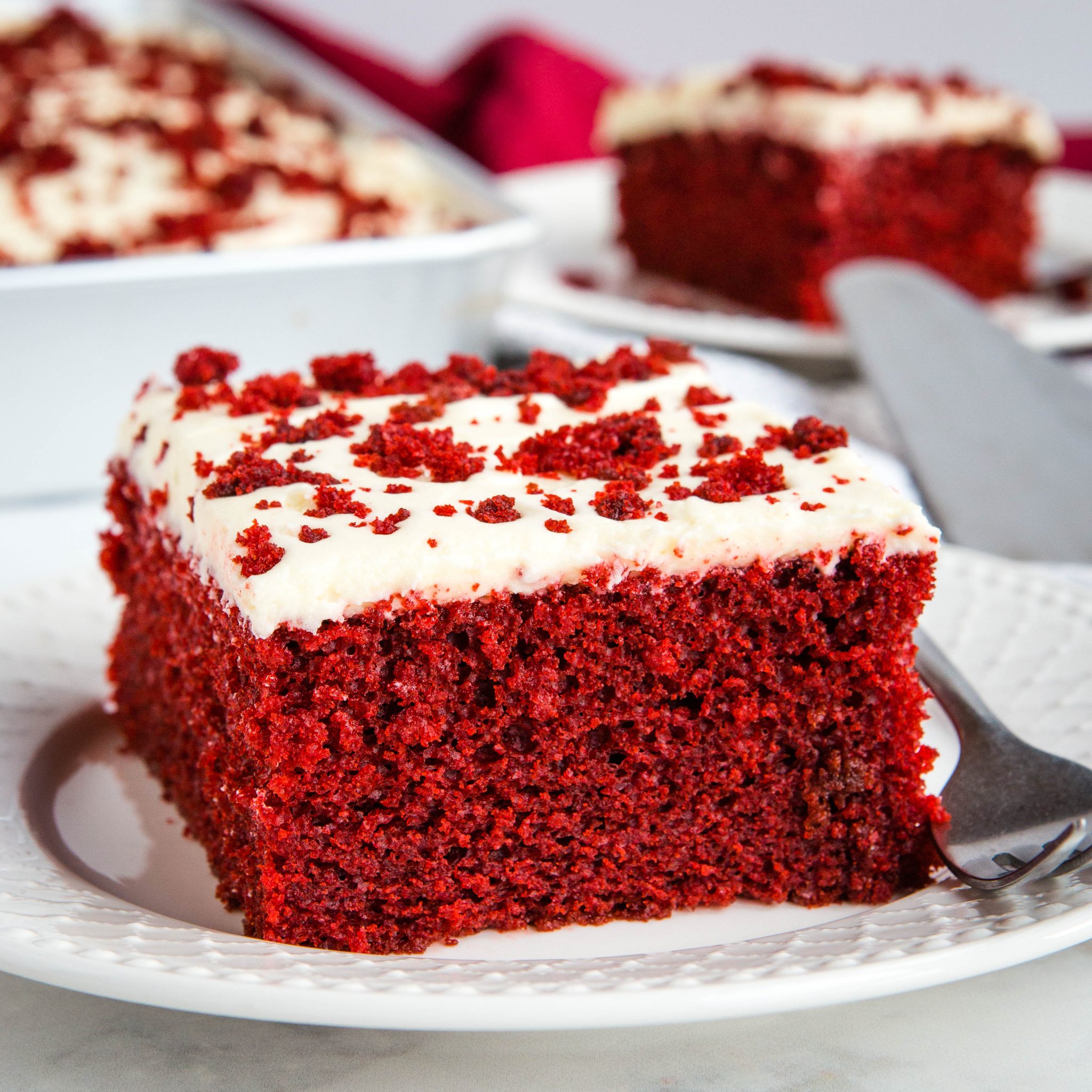 slice of homemade red velvet cake with cream cheese frosting on white plate