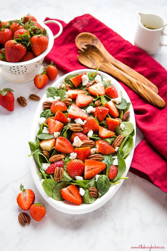 bowl of spinach and strawberry salad topped with pecans and goat cheese