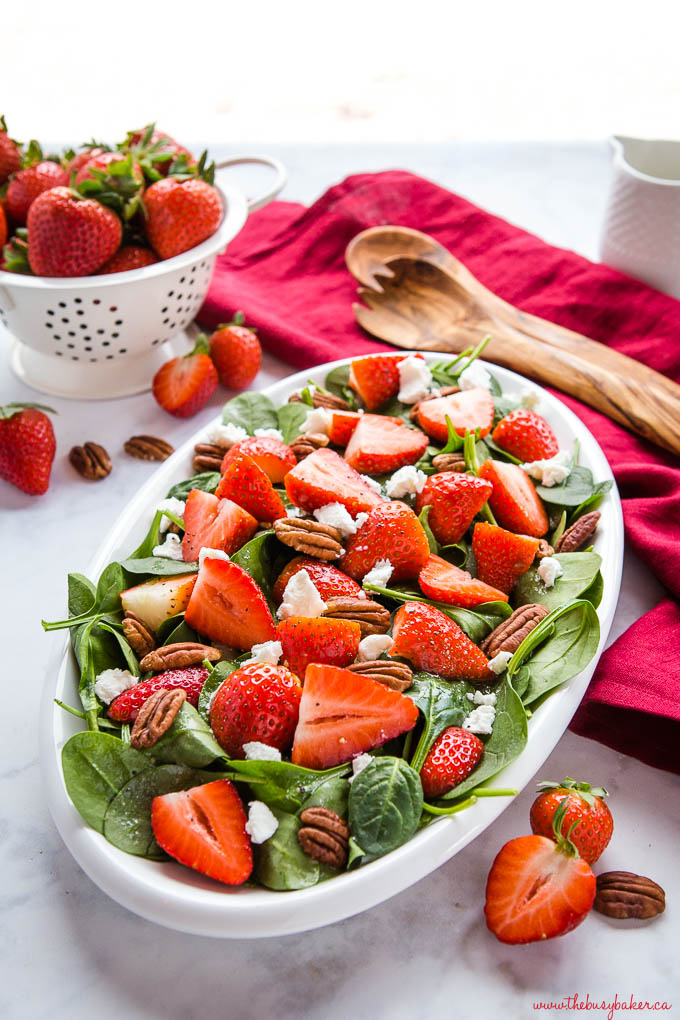bowl of spinach and strawberry salad next to basket of fresh strawberries