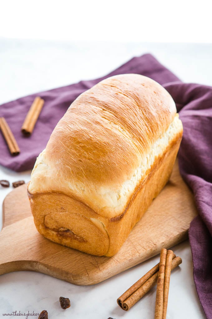 freshly baked loaf of homemade bread on cutting board with cinnamon sticks