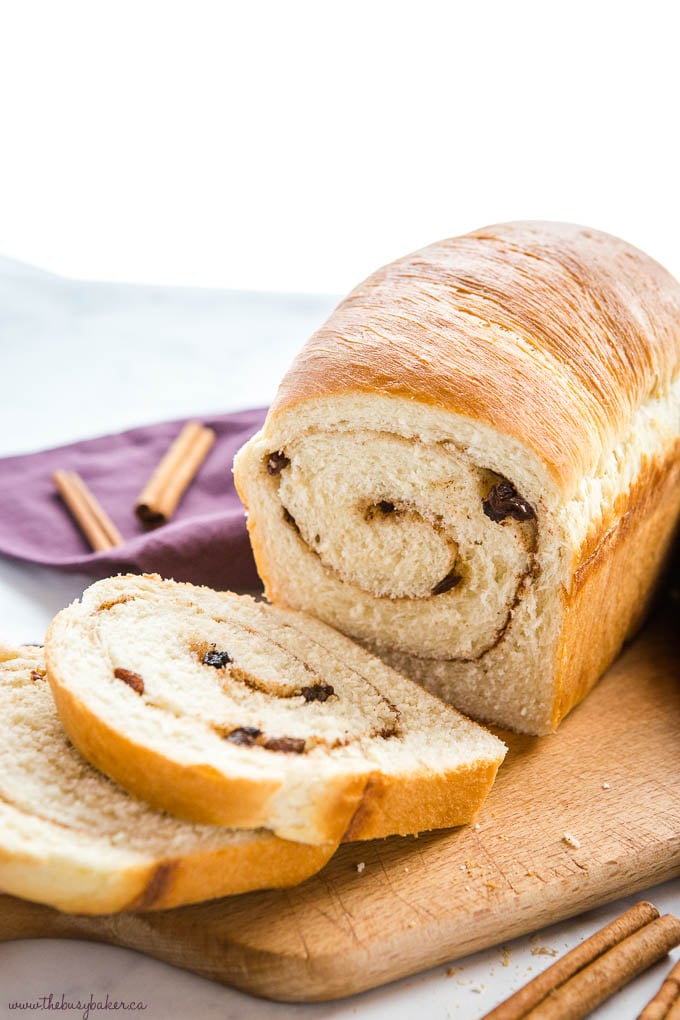 cinnamon raisin bread loaf with 2 slices cut from it on wood cutting board