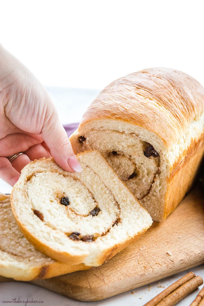 hand reaching for a slice of homemade bread with cinnamon and raisins in it
