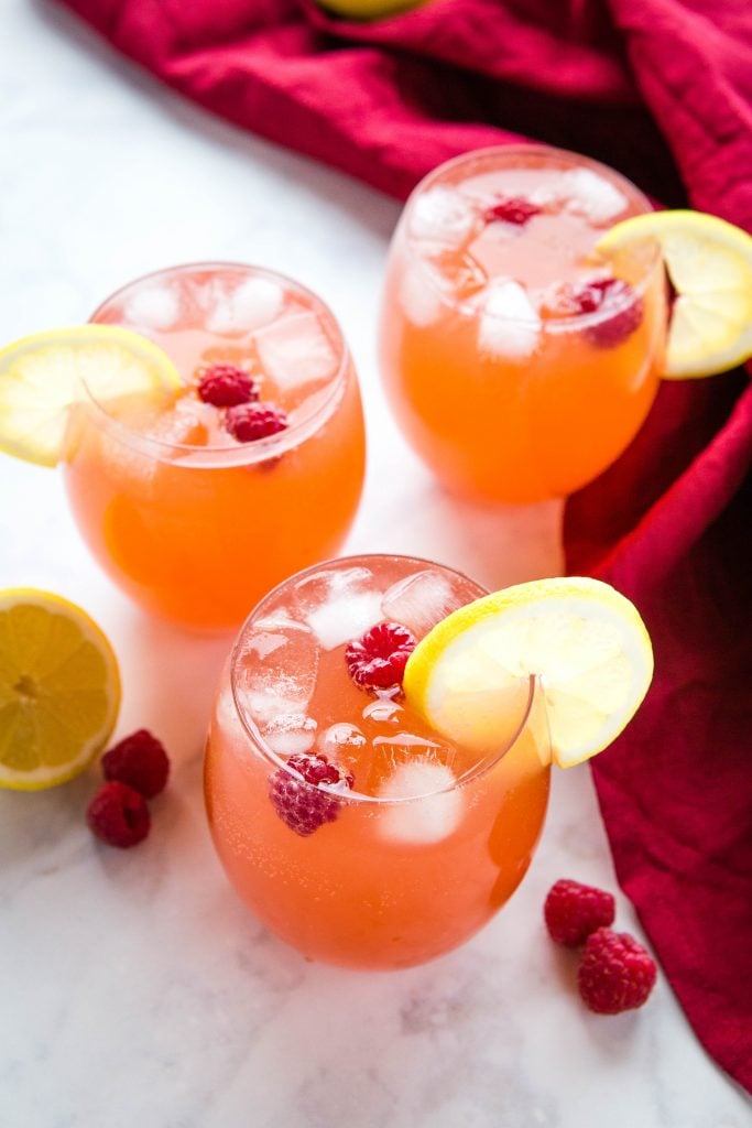 3 vasos llenos de hielo y ponche de frutas con rodajas de limón en el borde