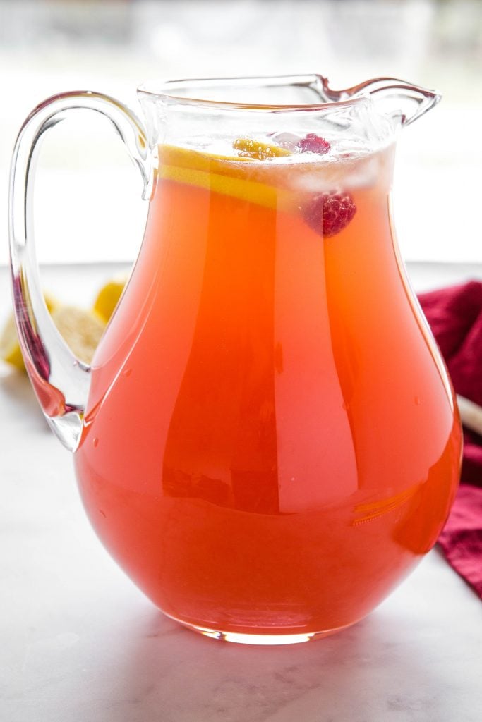 glass pitcher of red non-alcoholic punch with raspberries and lemon slices