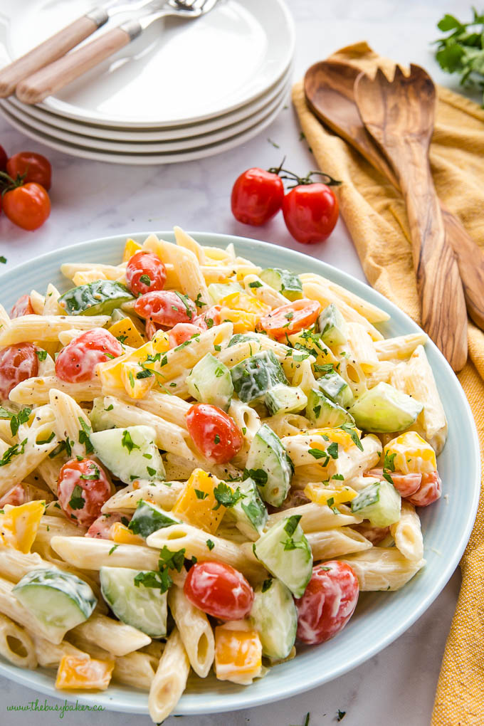 pasta salad with veggies in blue bowl with cherry tomatoes, cucumbers, and yellow peppers