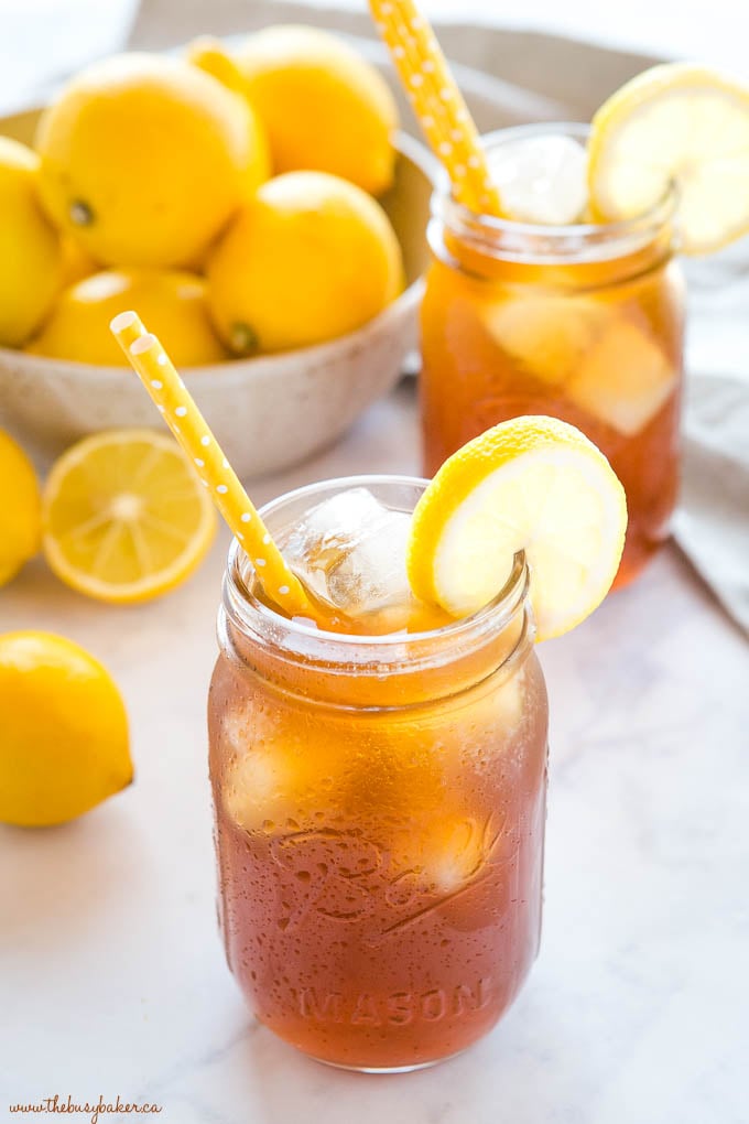 iced tea in mason jar with condensation and ice, with lemons and yellow straws