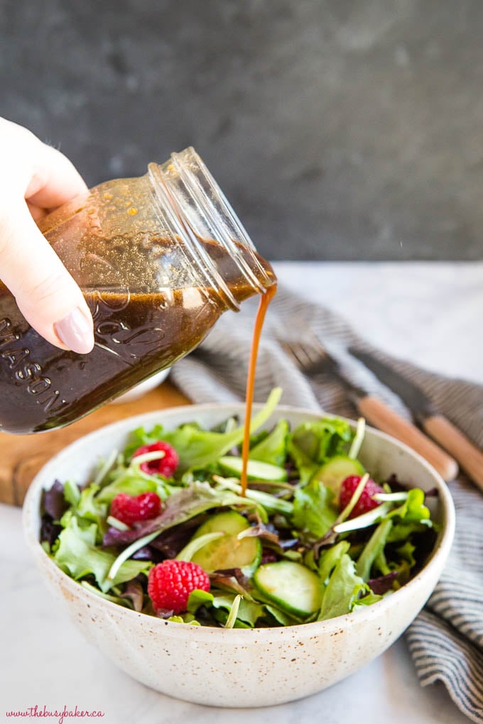 pouring maple balsamic vinaigrette over salad with raspberries and cucumbers