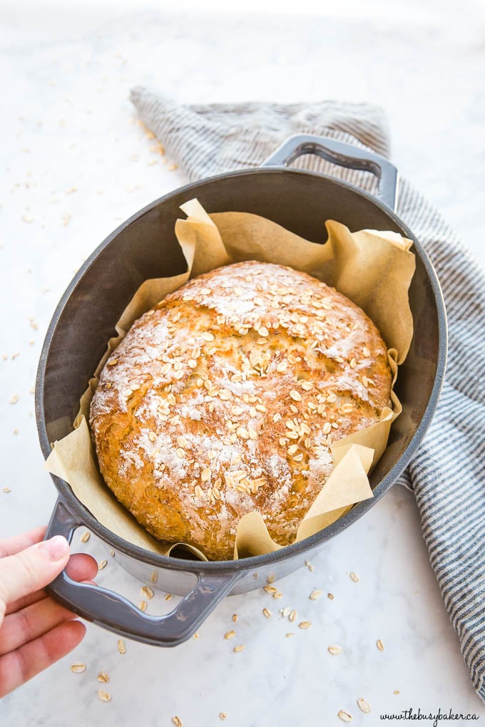 hand holding black dutch oven pot with loaf of honey oat bread
