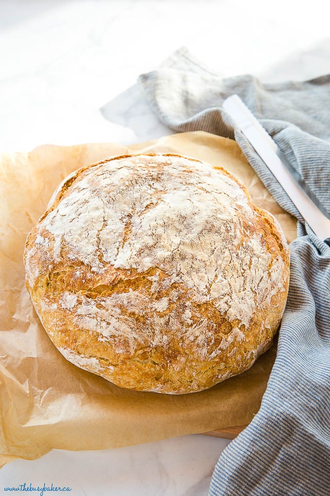 round loaf of crusty bread on brown parchment paper next to blue kitchen towel