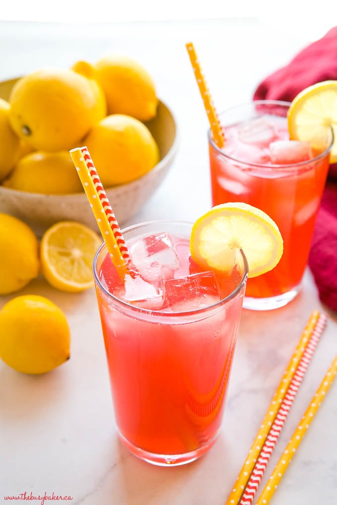 two glasses of pink lemonade with straws, ice and lemon slices