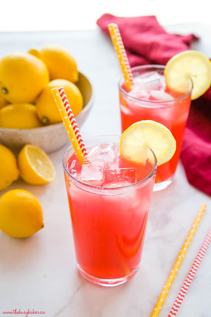 2 glasses of refreshing pink beverage over ice with striped paper straws and lemon slices on the rim