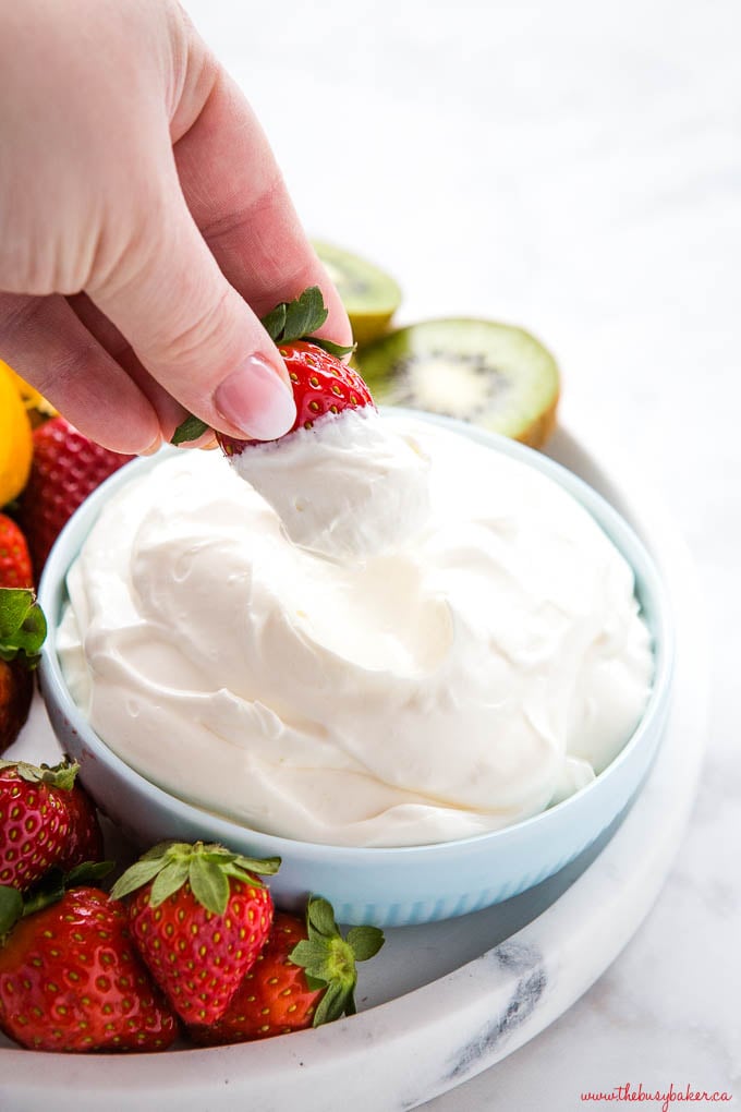 hand dipping strawberry into dessert fruit dip