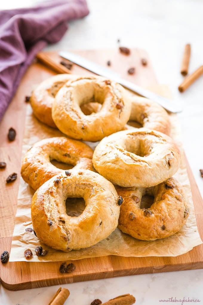 Cinnamon Raisin Bagels on wood cutting board with knife and cinnamon sticks