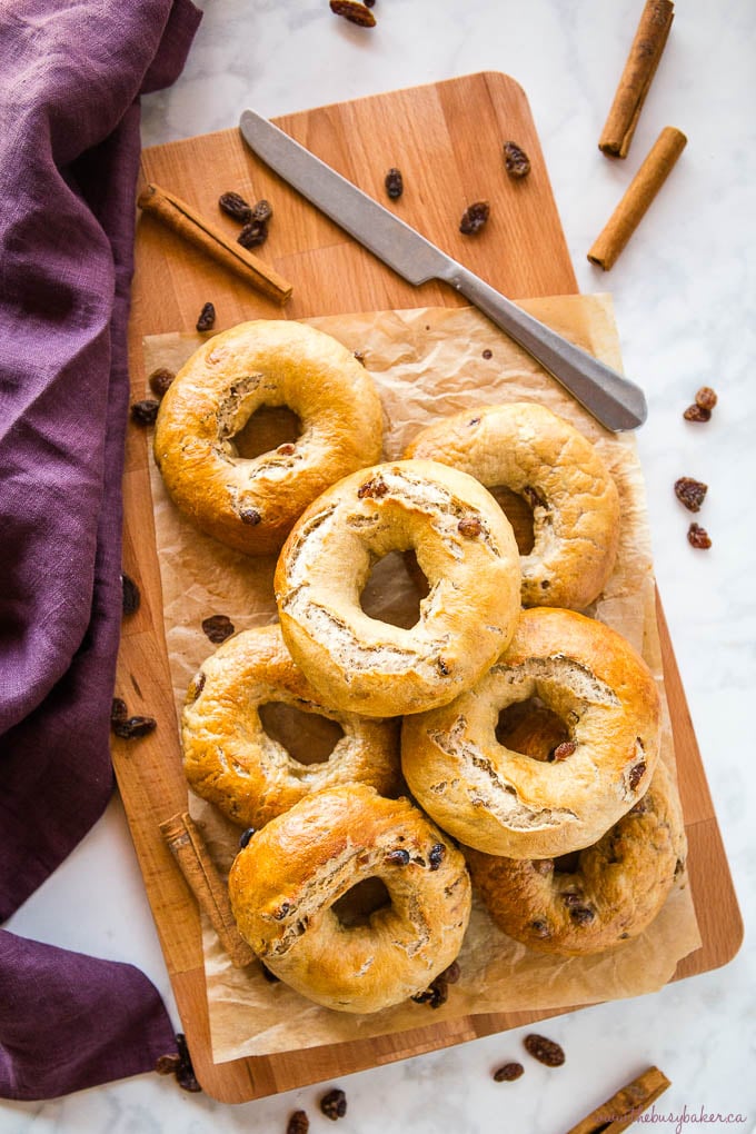 Cinnamon Raisin Bagels on wood cutting board with knife and cinnamon sticks