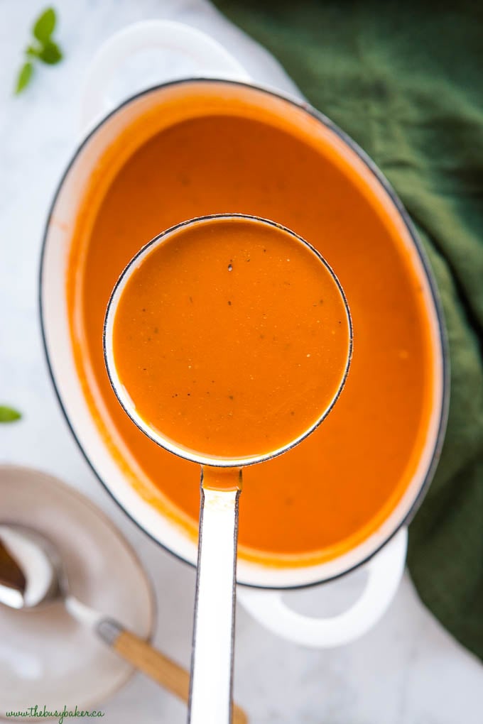 white ladle of homemade tomato soup with white cast iron pot