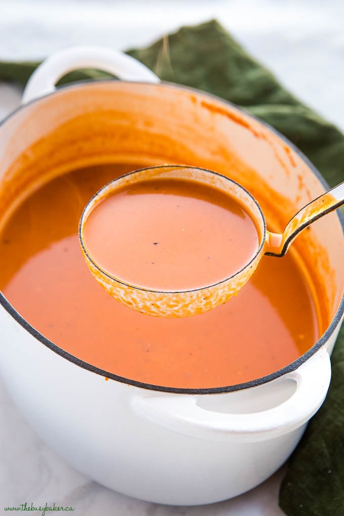 white ladle of creamy tomato soup in white cast iron pot