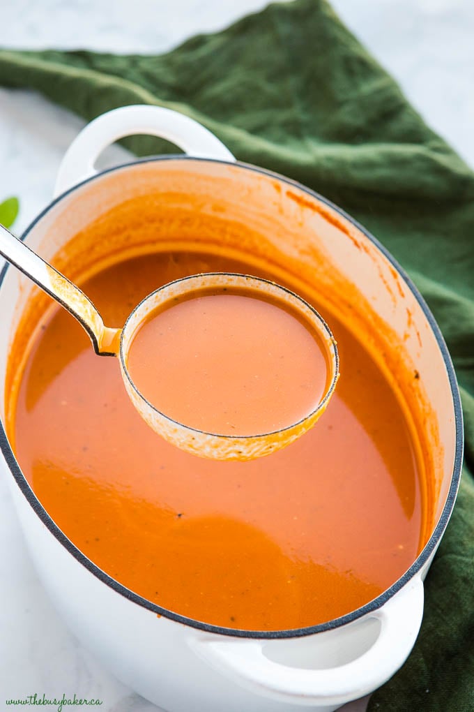 ladle of tomato soup in white pot 