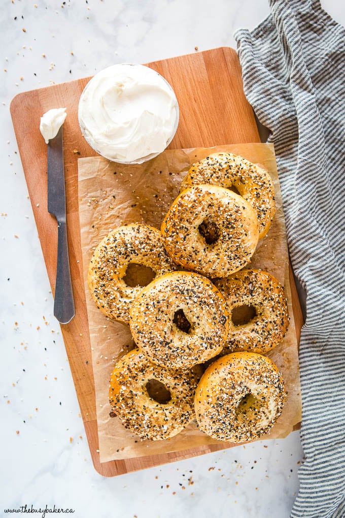 everything bagels on wooden cutting board with parchment paper and cream cheese