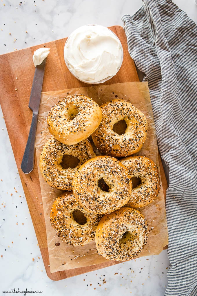 homemade everything bagels on wooden board with cream cheese on knife