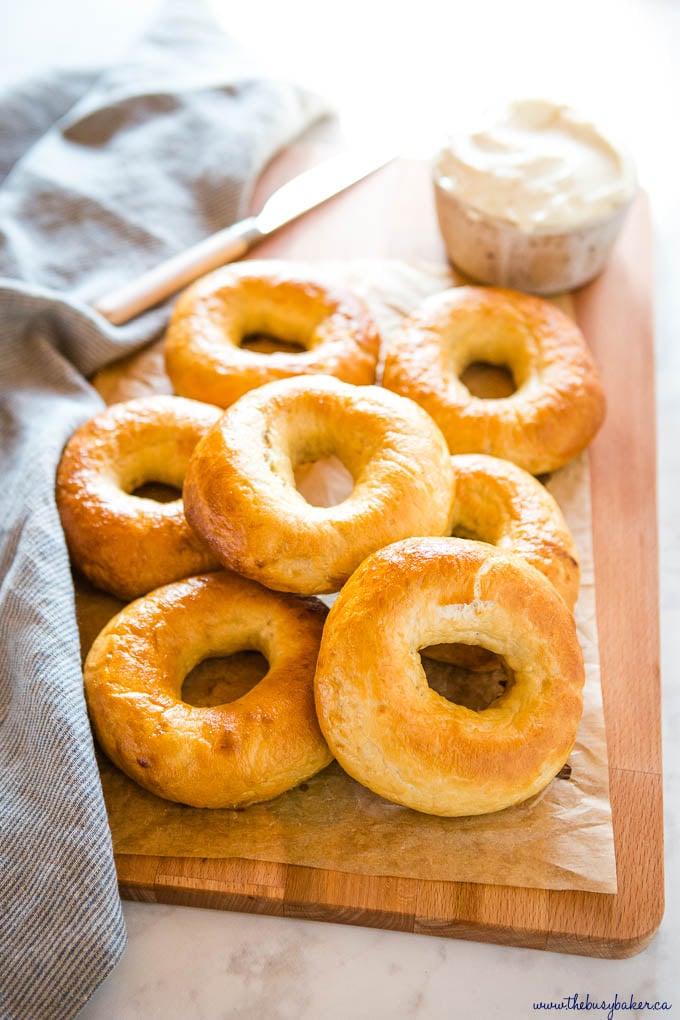 pile of new york-style bagels on wooden cutting board with cream cheese and a knife