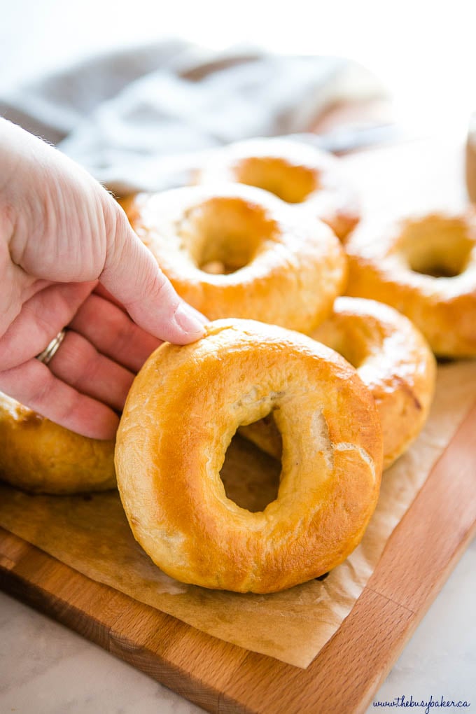 hand holding new york style bagel on wooden cutting board with parchment paper