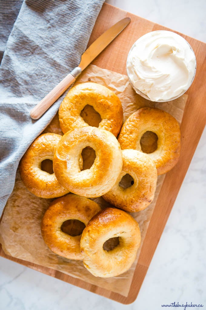 7 homemade new york-style bagels on wooden cutting board with cream cheese and a knife