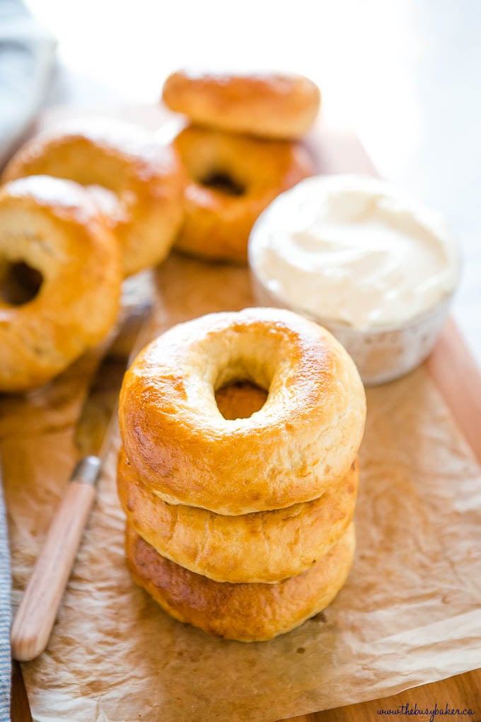 stack of 3 new york-style bagels on cutting board with parchment paper and cream cheese