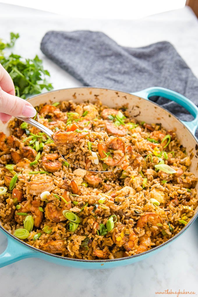 hand holding spoon of shrimp fried rice over cast iron pan