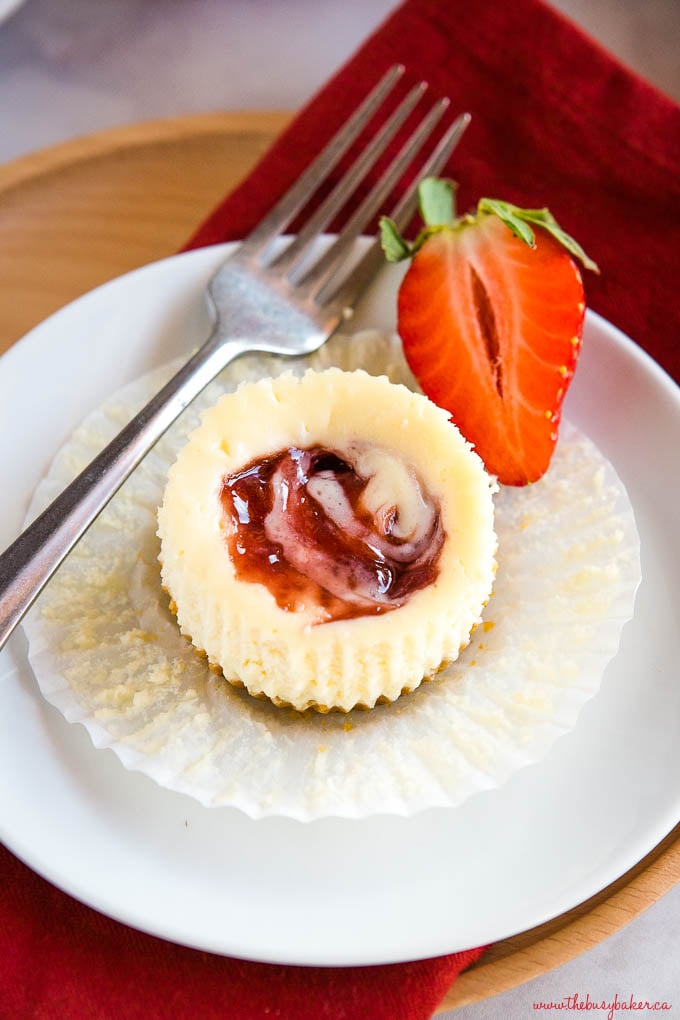 Mini Strawberry Swirl Cheesecake on white plate with a fork and a strawberry