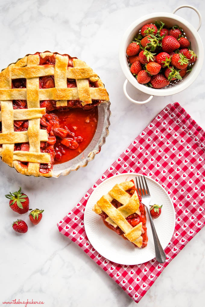 juicy strawberry pie with strawberries and slice of pie on a white plate