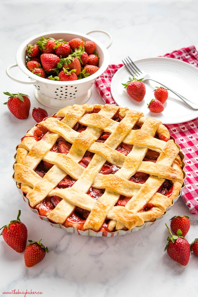 strawberry pie with golden lattice pie crust on a white marble counter with fresh strawberries