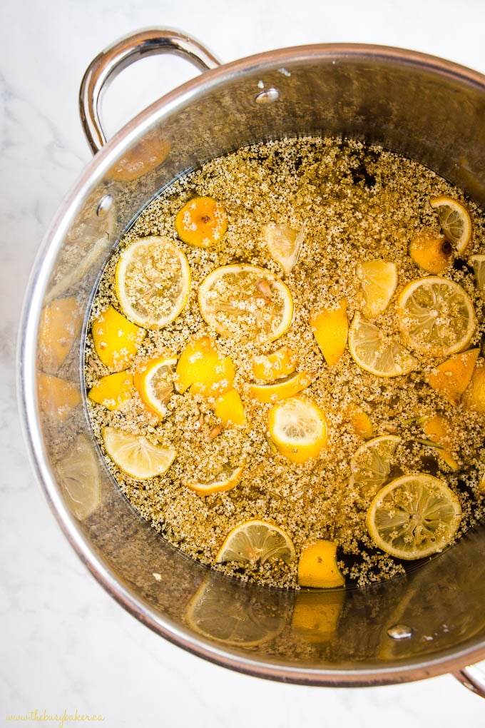 overhead image: elderflower blossoms, lemon slices and water in large stock pot to make elderflower syrup recipe.