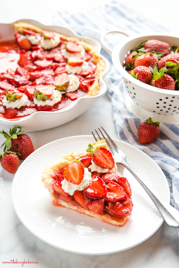 fresh strawberry pie slice on white plate with whipped cream and sliced berries