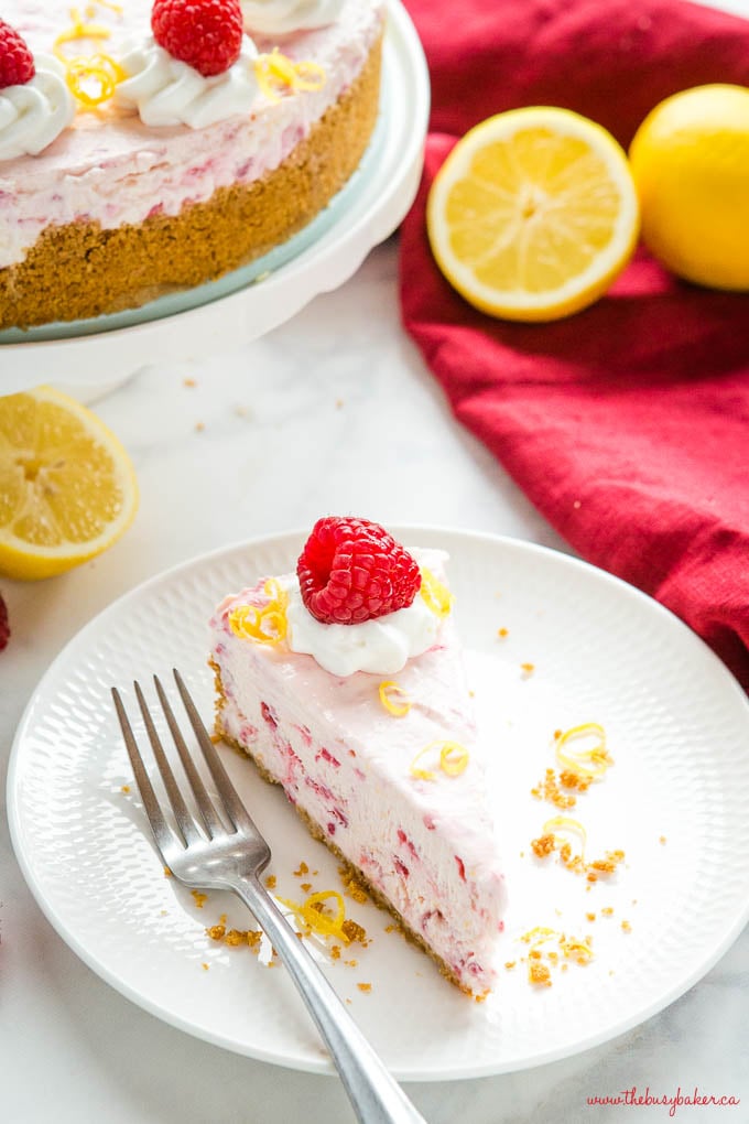 slice of lemon raspberry no bake cheesecake on white plate with fork and lemons