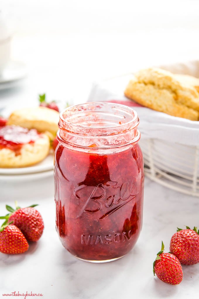 mason jar of strawberry jam on marble counter with scones in the background