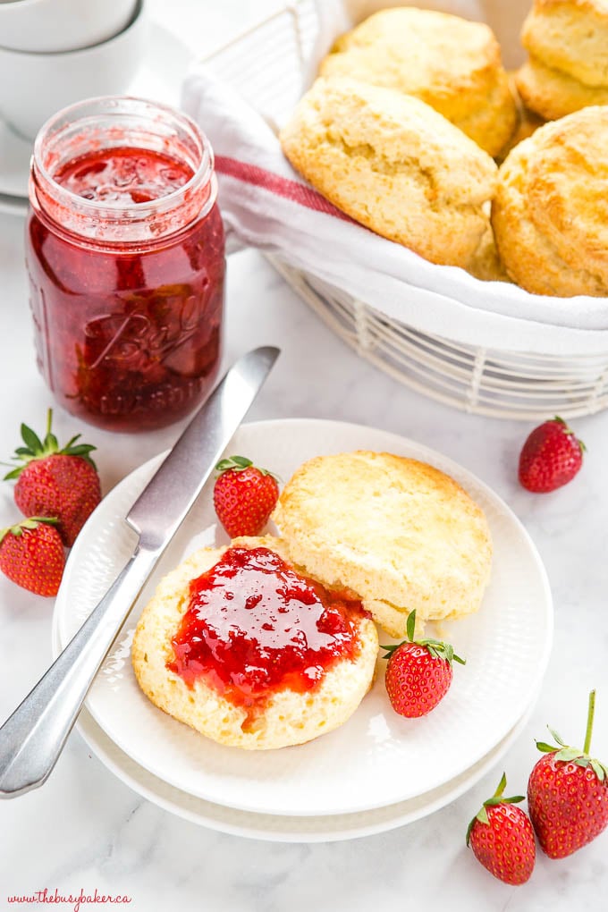 scone on white plate with strawberry jam, fresh strawberries, and a knife