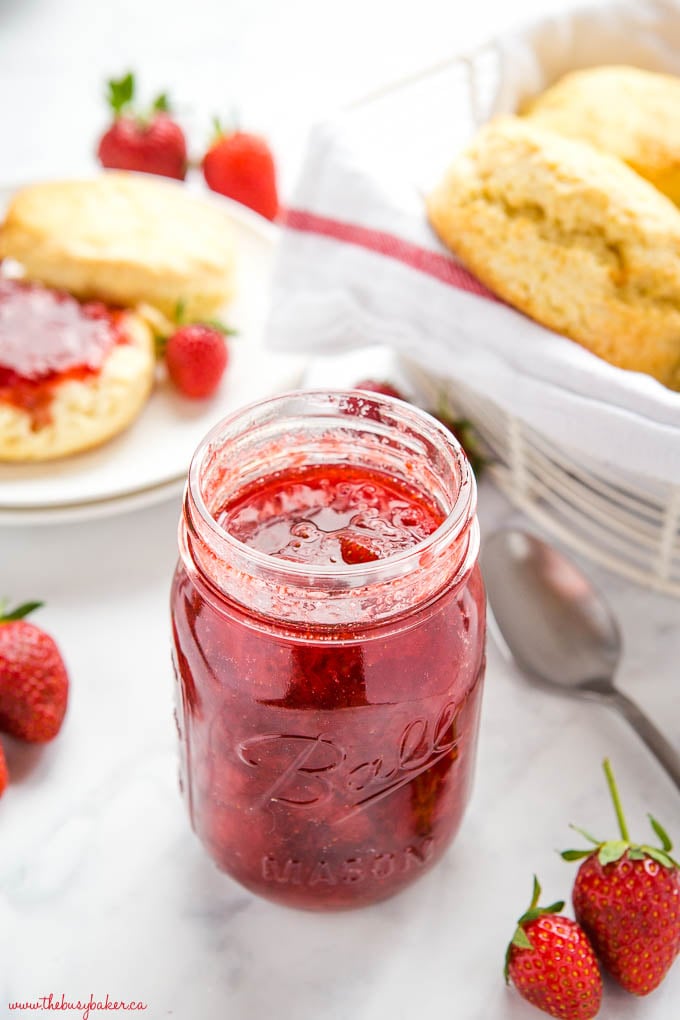 mason jar of strawberry jam with fresh strawberries, scones and a spoon