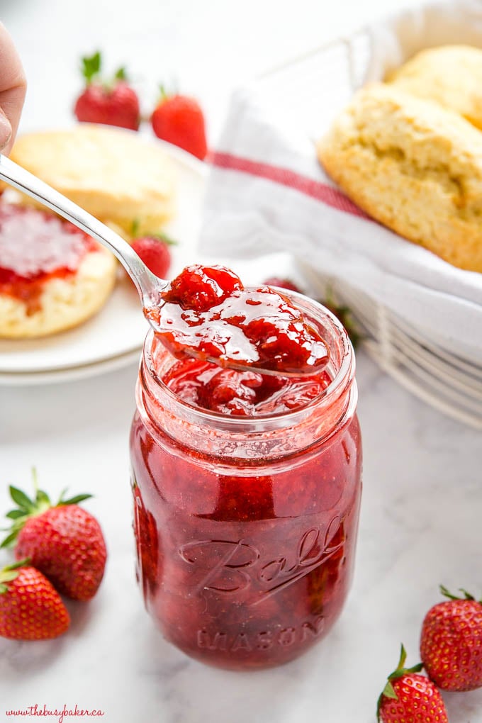 spoonful of strawberry jam with scones and jar of jam in the background