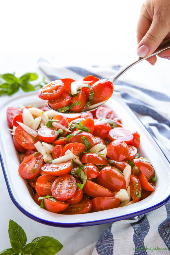 woman's hand holding spoon with tomato basil onion salad