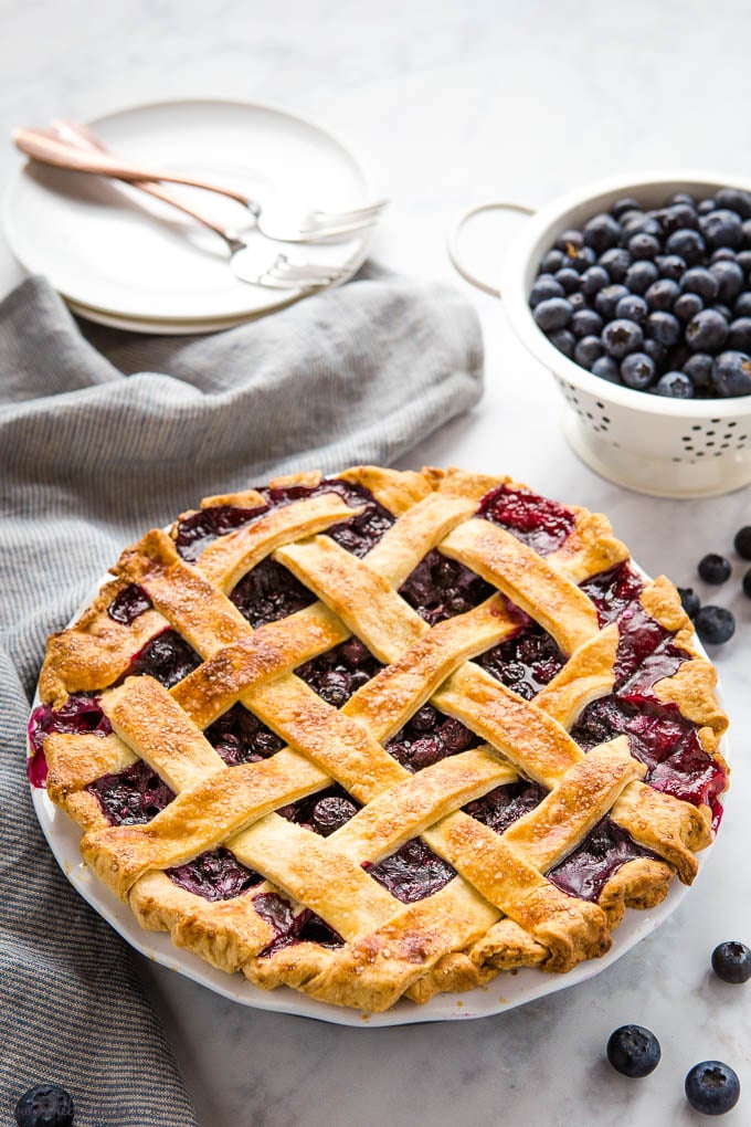 blueberry pie with fresh blueberries, dessert plates with forks and striped kitchen towel