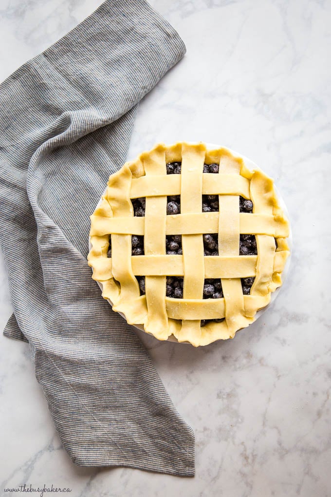 overhead image: unbaked blueberry pie with lattice crust, on a marble backdrop