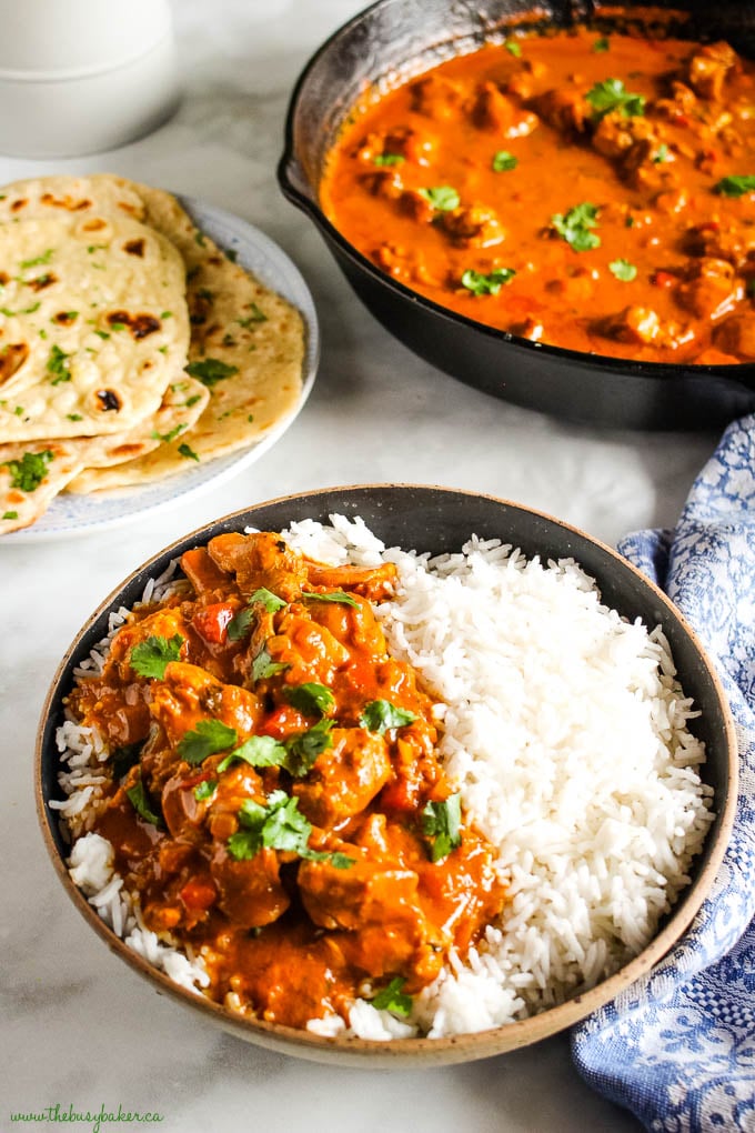 butter chicken with rice in black bowl with naan bread