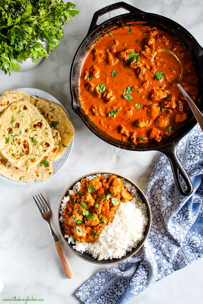 overhead image: cast iron skillet with butter chicken, a plate with naan bread, and butter chicken over rice in a black bowl