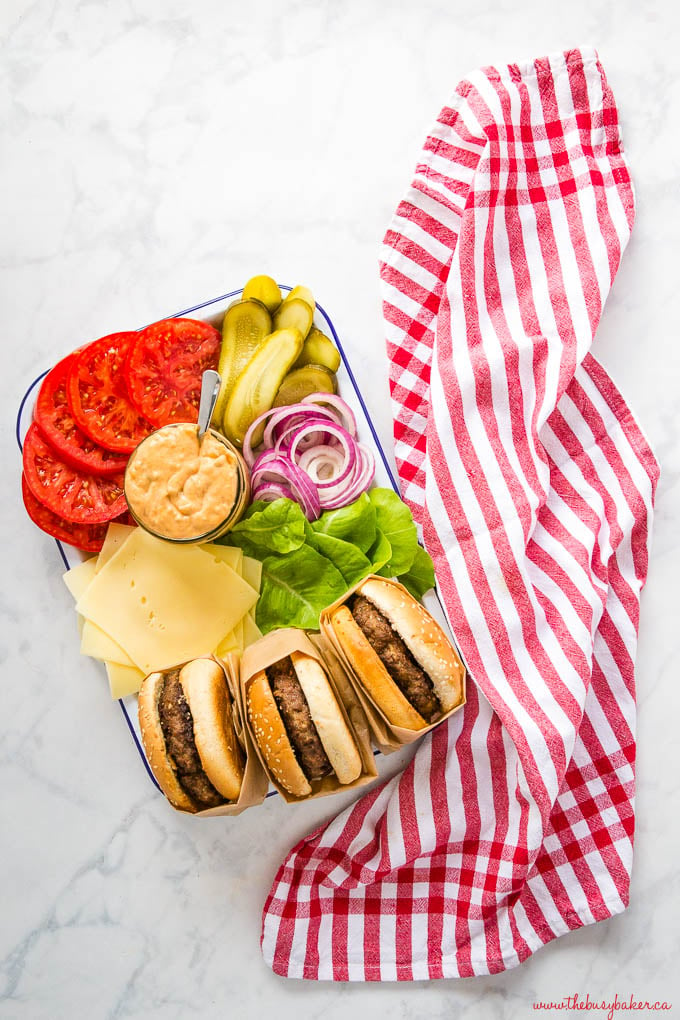 overhead image: platter of homemade burgers with sesame seed buns, lettuce, cheese, tomatoes, pickles, onions and burger sauce