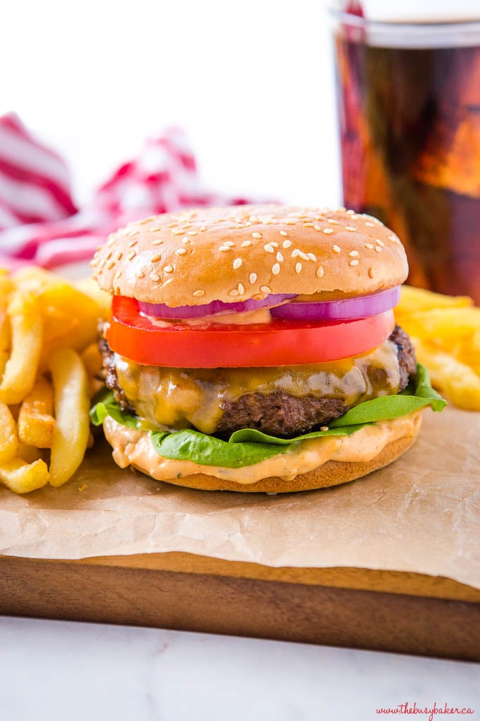 homemade burger on sesame seed bun with lettuce, tomato, cheddar cheese, onions and burger sauce