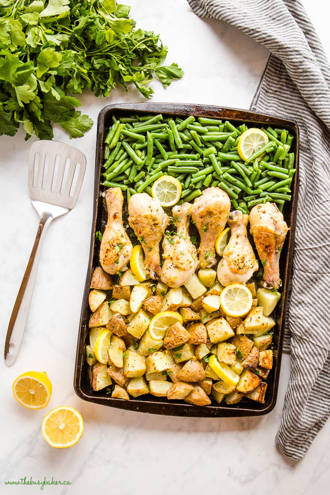 overhead image: sheet pan with lemon pepper chicken, green beans and potatoes, with lemon slices 
