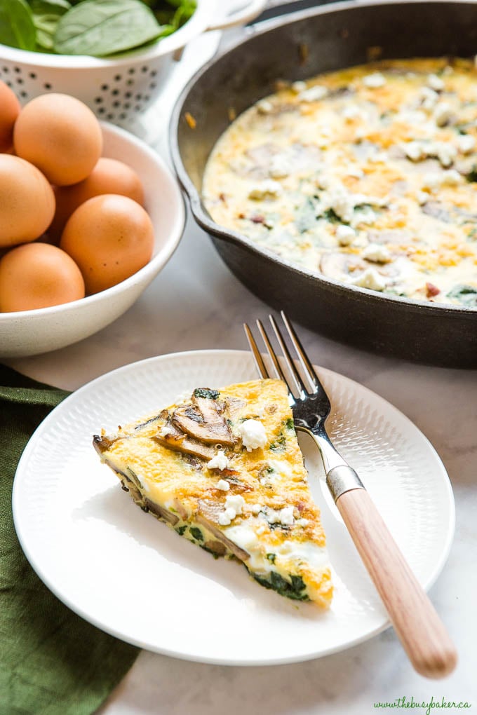 slice of mushroom spinach frittata with goat cheese on white plate with wooden fork