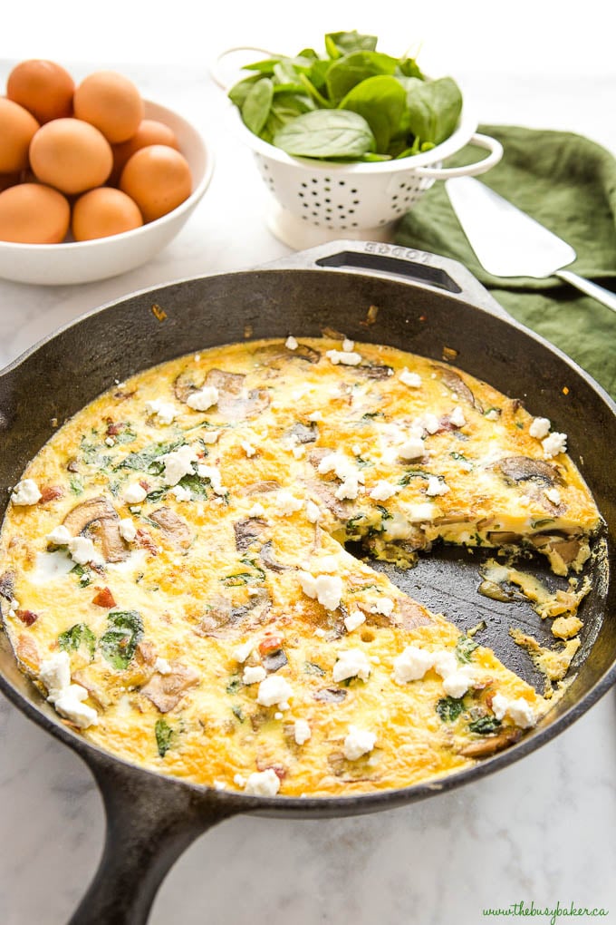 cast iron skillet with spinach mushroom egg frittata with a slice missing