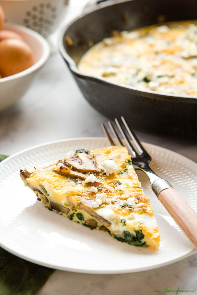 slice of mushroom spinach frittata on white plate with wooden handled fork